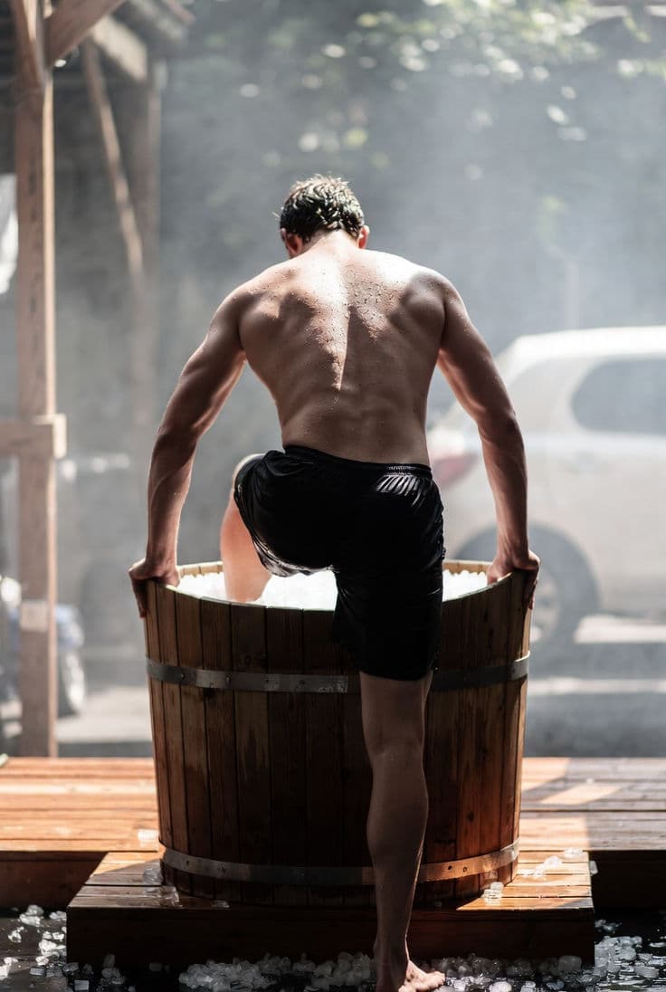 Homem entrando em banheira de imersão em água gelada ao ar livre, com vapor ambiente